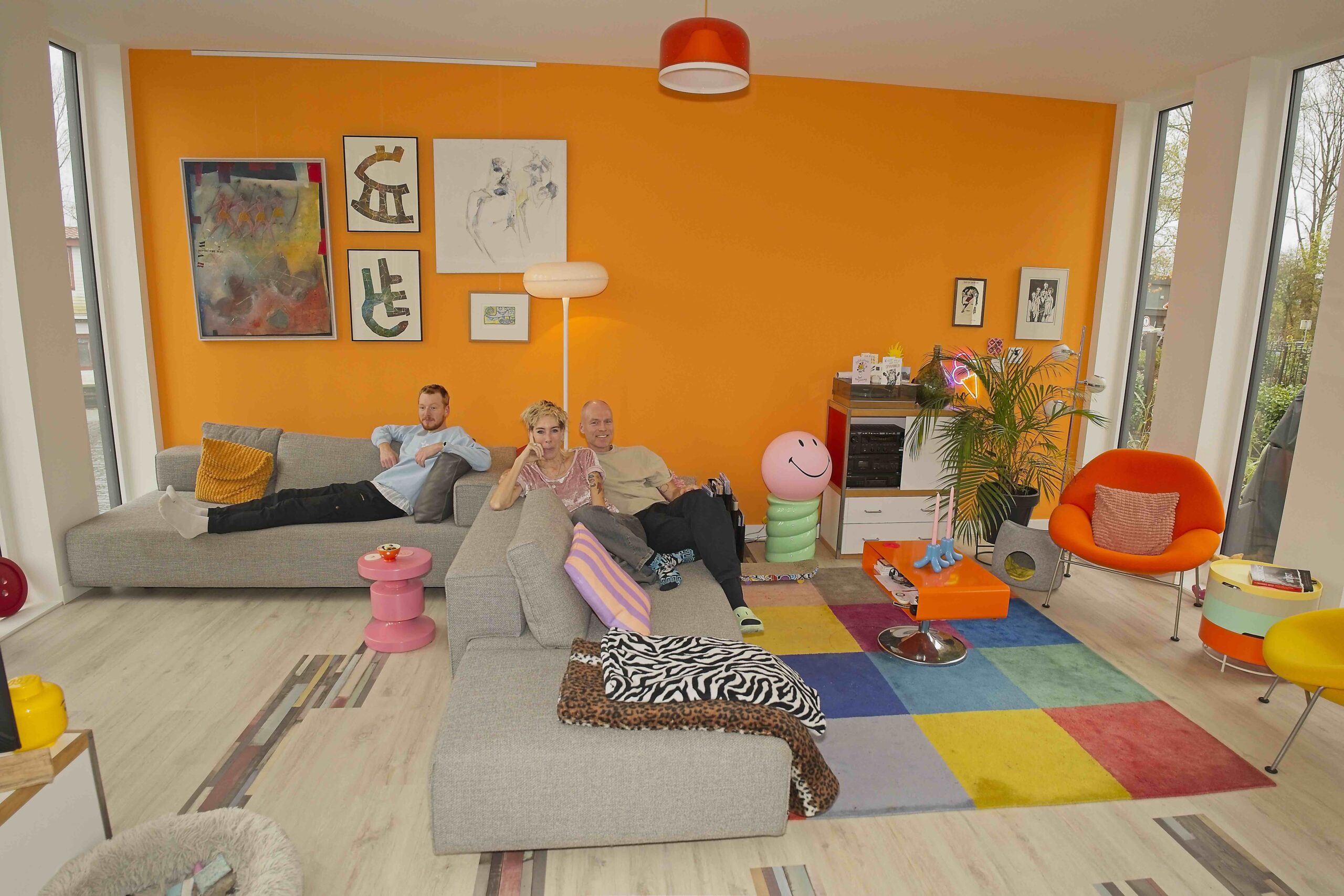 Jeroen, Inger en Demy op de bank in kleurrijke oranje woonkamer op hun woonark Friendship IJsbaanpad Amsterdam