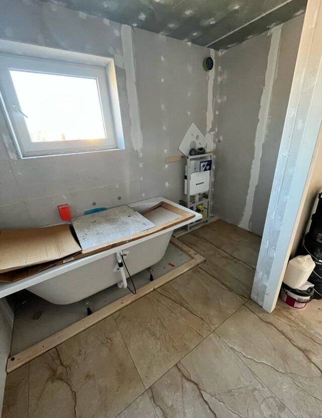 ~ De nieuwbouw van > Wendy ~ 
#blog 15 | Beton Ciré
Nu de vloer boven erin ligt en de mannen beneden alles hebben dichtgezet, kan ik door naar de volgende deadline: het aanbrengen van de beton ciré in de badkamer. Ook hier tikt de klok, want terwijl ik binnenkort voor werk een week naar het buitenland moet, staat in diezelfde week de montage van de badkamer gepland.

Alles moet inmiddels met een ladder naar beneden, dus met de zak betonmortel op mijn schouder daal ik dapper af—gelukkig zijn het er maar twee.
Ik begin vol goede moed met het aanmaken van de mortel die over twee wanden moet worden aangebracht. Keurig netjes breng ik een eerste laagje aan. Té netjes, zo blijkt. Het wapeningsgaas, dat je in de mortel drukt, blijft nergens aan plakken en glijdt net zo makkelijk weer van de muur—recht over mij heen, natuurlijk. Betonmortel in je haar, altijd feest. Maar bij poging twee, met een wat dikkere laag, lukt het gelukkig wel.

De volgende ochtend gaat de wekker absurd vroeg. Er moet nog minstens één laag betonmortel overheen, en als ik het strak plan, kan ik er 's avonds nog eentje doen. Want zondag moet ik echt starten met de eerste laag beton ciré, anders red ik het niet voor mijn vertrek. Werken met mortel is behoorlijk pittig. Mijn schouders zijn gewend aan een tennisbal of golfclub, niet aan het smeren van zwaar cement op de muur.

Opnieuw gaat zondag de wekker vroeg. Na die eerste grove laag ciré ga ik s’nachts direct door met de tweede, wat een klus. Maar eerlijk? Ondanks de verzuurde schouders en blaren op mijn handen, is het eigenlijk ontzettend leuk werk. Je ziet het resultaat meteen ontstaan, in tegenstelling tot dat eindeloze schuren en plamuren.

Met spierpijn, ruwe handen en wallen tot aan m’n kin stap ik een paar dagen later in het vliegtuig. Maar eerlijk is eerlijk: ik heb nog nooit zó uitgekeken naar een vlucht van dertien uur. Dertien uur waarin ik niets hoef behalve een beetje films kijken en slapen. Heerlijk.

@boot.wendy
~~~
#nieuwbouwproject #woonark #woonboot #arkenbouwer #bouwproject #nieuwbouw #houtskeletbouw #waterwonen #woonarkbouwen #betonbak #betoncire #betonciré #diy #betonmortel #badkamer